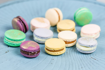 Fototapeta na wymiar Close-up colorful French or Italian macaron on blue wooden table. Macarons is French dessert served with tea or coffee. wallpaper, Horizontal photo