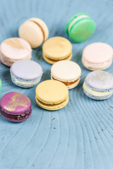 Fototapeta na wymiar Close-up colorful French or Italian macaron on blue wooden table. Macarons is French dessert served with tea or coffee. wallpaper, Vertical photo