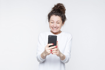 Excited female model receives unexpected message or news on telephone, looks joyfully into gadget, has overjoyed expression. Positive young happy woman views funny instagram photos on mobile phone.