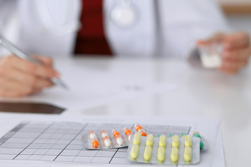Female medicine doctor fills up  prescription form to patient closeup. Panacea and life save,...