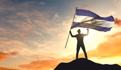 El Salvador flag being waved by a man celebrating success at the top of a mountain. 3D Rendering - obrazy, fototapety, plakaty