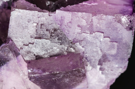 Fluorite surface closeup. Cubic crystals of fluorspar, a mineral form of calcium fluoride, CaF2. Colorful pink and purple crystal cluster. Isolated macro photo from above on black background.