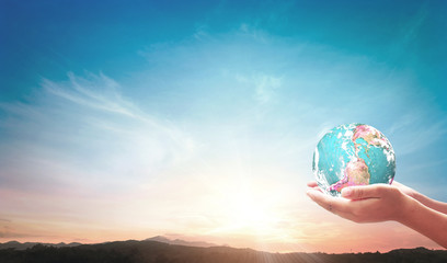 World environment day concept: Two human hands holding earth globe on mountain sunset background. Elements of this image furnished by NASA