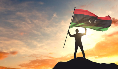 Libya flag being waved by a man celebrating success at the top of a mountain. 3D Rendering - obrazy, fototapety, plakaty