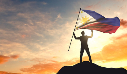 Philippines flag being waved by a man celebrating success at the top of a mountain. 3D Rendering © ink drop