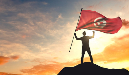 Tunisia flag being waved by a man celebrating success at the top of a mountain. 3D Rendering