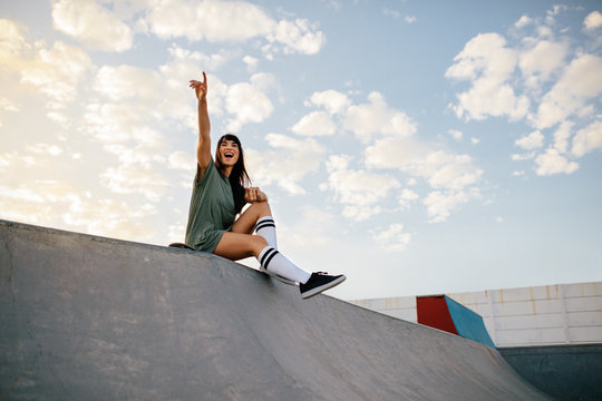 Woman sitting on skateboard ramp at skate park