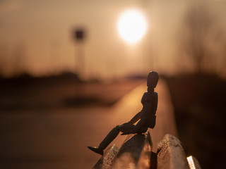 Wooden mannequin sitting on a wooden bench at sunset in a cloudy day