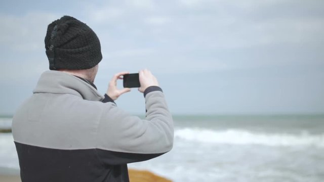 Young caucasian man taking photos of sea at storm 