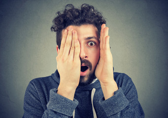 young man looking shocked, surprised in disbelief, with hands on face