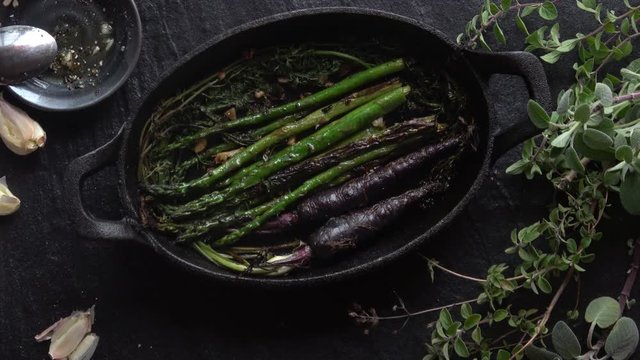 Roasted Asparagus and Purple Carrots in Cast Iron Skillet. Footage on black background with fresh herbs.