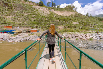 Fototapeta na wymiar Woman seen from behind crosses a suspension bridge over the Colca River, in the province of Arequipa, Peru