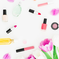 Frame with tulips flowers and cosmetics with perfume on white background. Top view. Flat lay feminine desk.