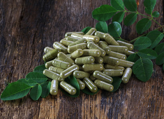 Herbal capsules from moringa leaf on wooden