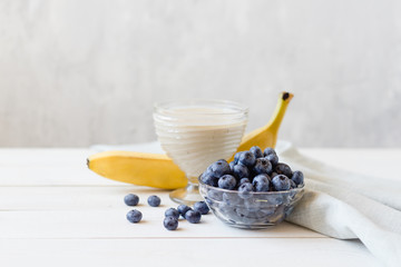 Banana smoothies and ripe blueberries in a glass bowl on a light background.