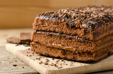 Chocolate cake. Biscuit dessert with chocolate powder with chocolate bar on a wooden background