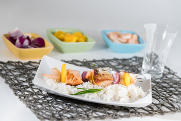 Fischspieß angerichtet auf einem Teller mit Reis mit den Zutaten in Schälchen