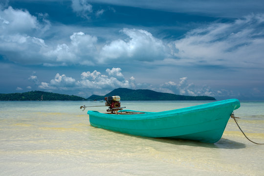 Turquoise motor boat on the beach with engine on the back, clear water mountain in the background. Beautiful weather with blue sky. Koh Rong Samloem island, Cambodia 