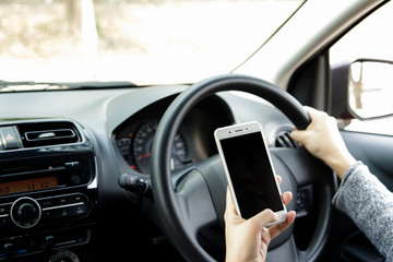 Woman hand holding mobile phone sending a text while driving a car. Selective focus.