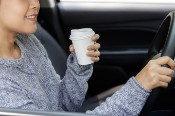 Young asian woman in casual wear driving a car and drinking coffee.  Woman sitting in car with coffee. Business woman multitasking.