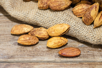 almond nuts on wooden table with almonds in gunny sack background, close up shot