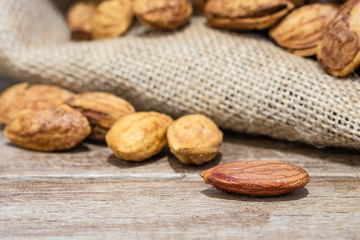 almond nuts on wooden table with almonds in gunny sack background, close up shot