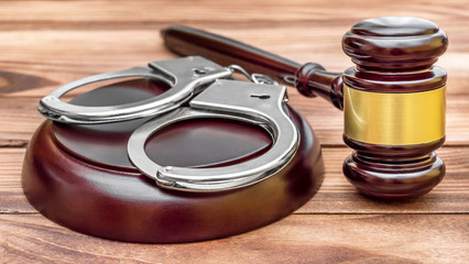 Judge's gavel with stand and handcuffs on wooden table.