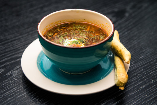 Soup with meat, olives, herbs, lemon in white bowl, black bread and spices on dark background,  homemade food. Traditional Russian soup - solyanka