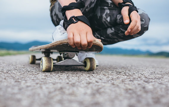 Boy sits on the skateboard legs and hands closeup image