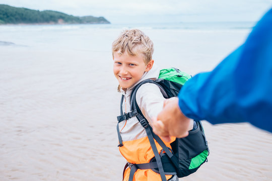 Backpacker boy traveler takes his father hand on the ocean coast