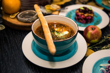 Soup with meat, olives, herbs, lemon in white bowl, black bread and spices on dark background, ...