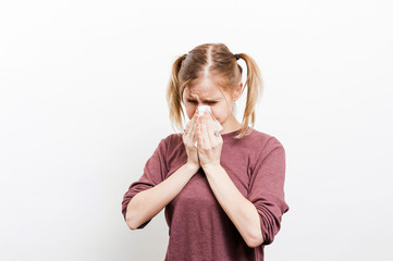 Sneezing and blowing her nose, a young woman struggles with a head cold. Young sick woman