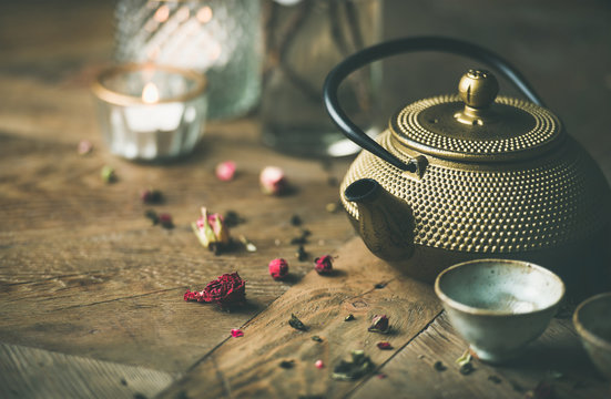 Traditional Asian tea ceremony arrangement. Golden iron teapot, cups, dried rose, candles over vintage wooden table background, selective focus