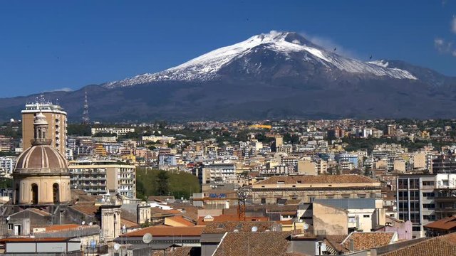 Catania and snowy mount Etna on blue sky background. Sicily islend, Italy.