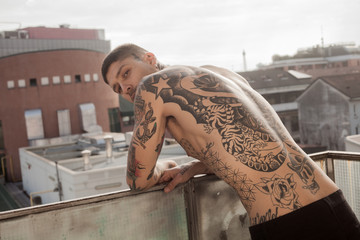 Handsome tattooed man back portrait posing on balcony and looking at camera