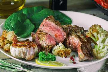 Steak rare with the blood of vegetables tomatoes and spinach grilled in a pan at home on the wooden table. Rustic style.