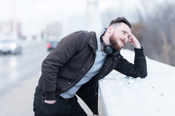 Portrait of a thinking handsome young hipster man while leaning on the bridges railing.