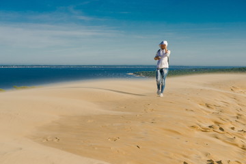 tourist in the desert. girl traveler takes pictures of desert sands on a mobile phone. Woman tourist in a white jacket walking on sand. wind in the desert. Pilat Dune
