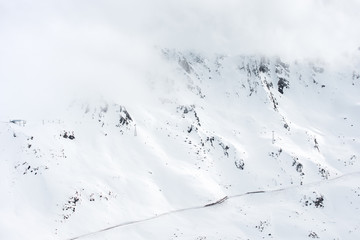 Mountain landscape. Fog and clouds on top. Snow-covered slopes and mountain road