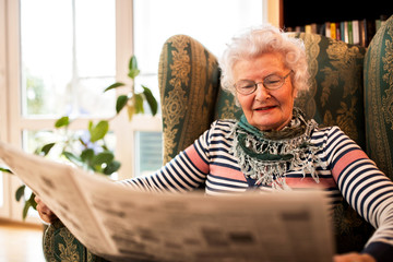 Senior woman in pansion relaxing at home while reading a newspaper