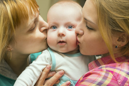 two women kiss the baby