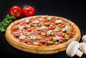 Delicious tasty pizza with mozzarella, sausages, cucumber, pepper and sauce on wooden board on dark background