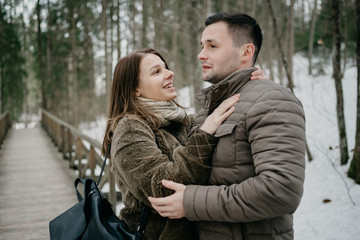 Stylish man with his attractive young wife embrace in the forest on the wooden bridge.