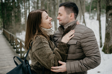 Stylish man with his cute young wife smiling and embrace in the forest on the wooden bridge.