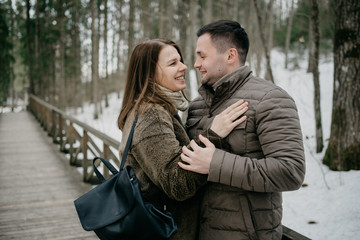 Stylish man with his attractive young wife smiling and embrace in the forest on the wooden bridge.