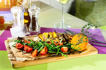 Delicious fish served with tomatoes, lemon and herbs on the wooden board at a cafe. Selective focus