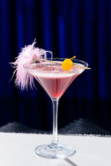 Alcoholic pink cocktail in a martini glass with straw on blue background, shallow dof