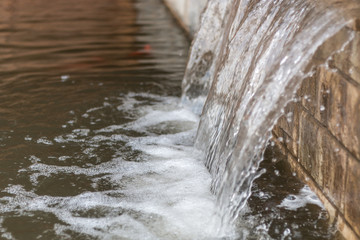 Waterfall on old brown stonewall. Running water cascade streaming in city river. Close up.