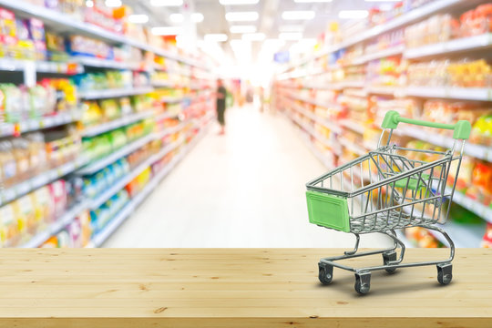 Mini Shopping Cart On wood with blur background supermarket shelves. Shopping online concept.