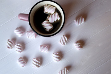 The pink mug of hot coffee with marshmallow on a white wooden table.